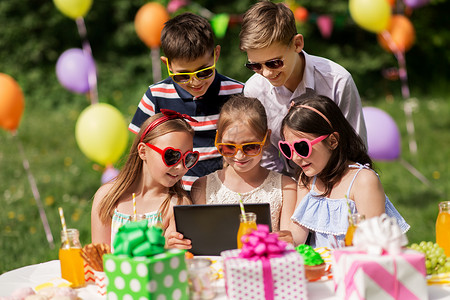假期,童技术快乐的孩子戴太阳镜与平板电脑生日聚会夏季花园生日派上平板电脑的快乐孩子背景图片