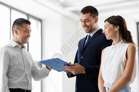 房地产业务,销售人的男房地产经纪人与剪贴板笔合同文件给客户新的办公室经纪人向客户出示合同文件背景图片