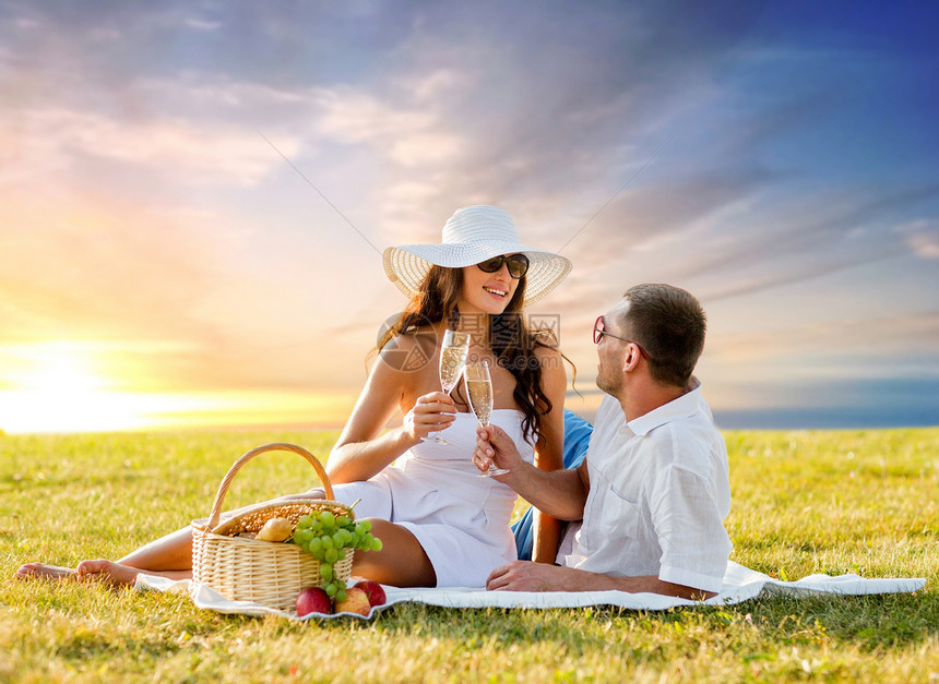 爱情,约会,人庆祝的微笑的夫妇草地上的日落天空背景上野餐时喝香槟微笑的夫妇野餐时喝香槟图片