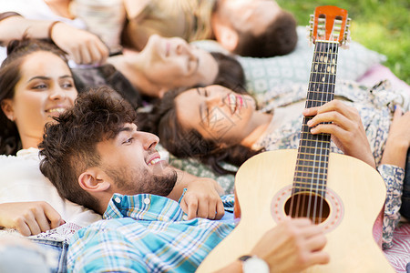 友谊,休闲夏天的群快乐的微笑的朋友弹吉他,野餐毯子上冷却朋友们弹吉他,毯子上发冷背景