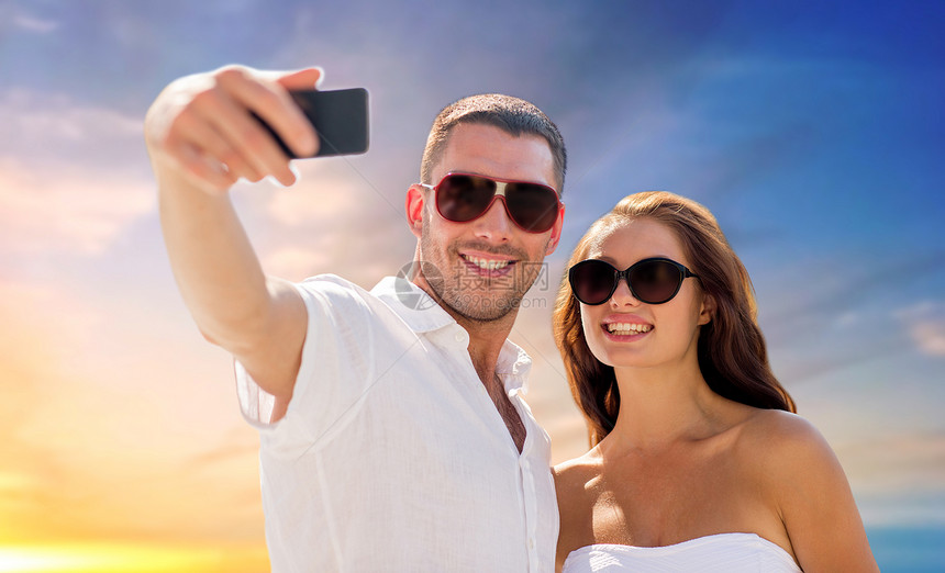 爱,夏天技术微笑的夫妇太阳镜,智能手机天空日落背景下自拍夫妇日落的天空上用智能手机自拍图片