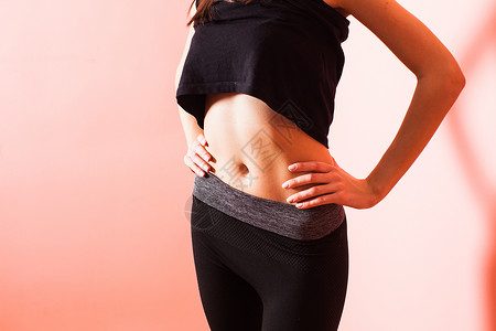 抠肚脐穿着深色运动服的运动女孩展示按压的胃运动身材的女孩背景