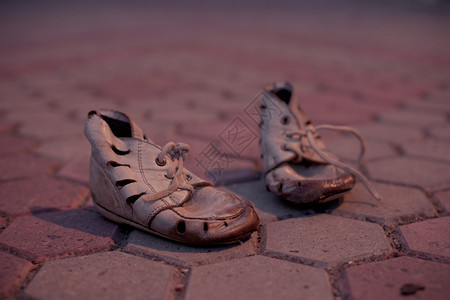 人行道瓷砖上破旧的婴儿鞋贫穷的可怜孩子的旧鞋背景图片