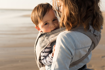 吊索妈妈带着孩子母亲带着麦格宝宝海滩上抱着蹒跚学步的孩子背景