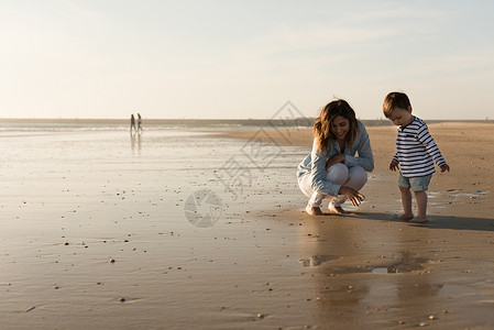 妈妈蹒跚学步的孩子海滩上轻的母亲蹒跚学步的孩子探索海滩图片