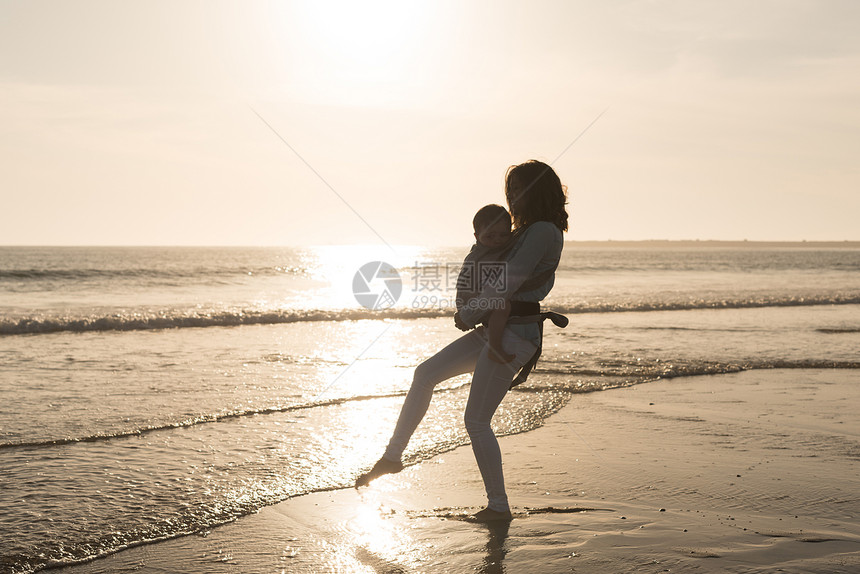 母亲带着麦格宝宝海滩上抱着蹒跚学步的孩子图片