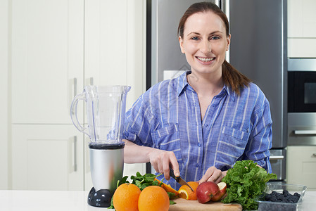 女人切水果放进榨汁机的肖像背景图片