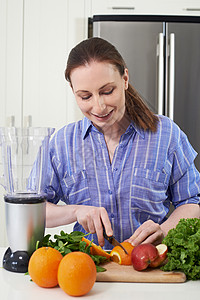 厨房里的女人切水果放进榨汁机里图片