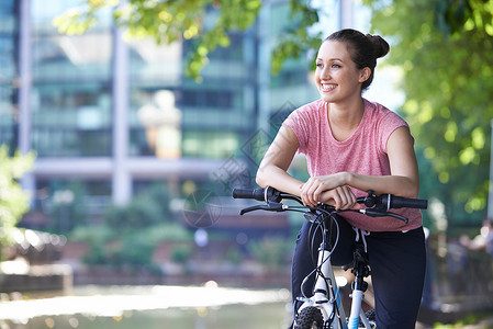 轻女子城市环境下骑自行车河边图片