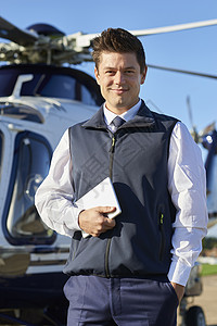 微笑飞行员站直升机前与数字平板电脑的肖像图片