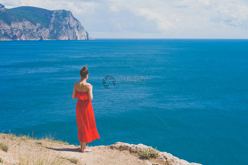 户外生活方式照片的女人穿着红色的衣服看着大海旅行背景旅游业图片