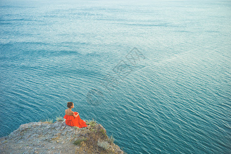户外生活方式照片的女人穿着红色的衣服看着大海旅行背景旅游业图片