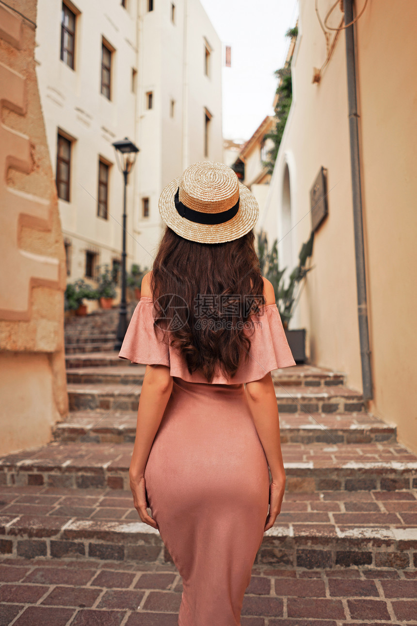 美丽的黑发轻女子,穿着粉红色的连衣裙草帽,走欧洲老城的街上时尚风格暑假旅行图片