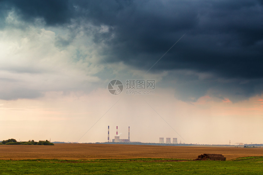 暴风雨戏剧云下发电厂的全景日落时分的发电站金色的麦田图片