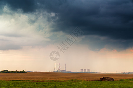 暴风雨戏剧云下发电厂的全景日落时分的发电站金色的麦田图片