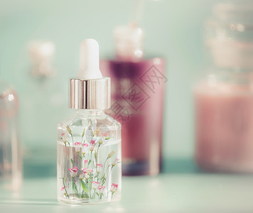 透明化妆瓶,液体,吸管小粉红色的花花精草药提取物血清桌子上,正视图美容现代护肤理念背景图片