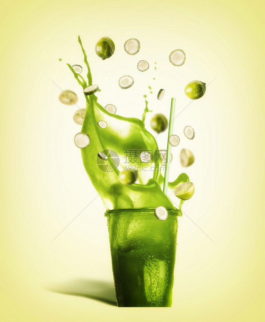 璃与饮用吸管绿色飞溅夏季饮料冰沙,果汁柠檬水与飞行成分柠檬黄瓜片黄色背景,正视图图片