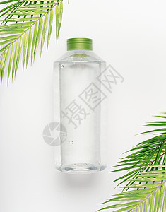透明液体瓶与绿色盖子白色书桌背景与热带棕榈叶,顶部视图图片
