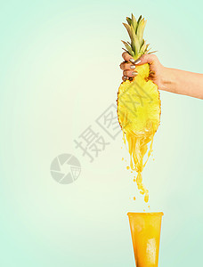 菠萝汁的女手着半的菠萝,阳光明媚的蓝色背景下把果汁压成璃夏季饮料飞溅背景图片