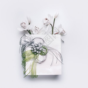 白色桌背景上绿色丝带兰花花的纸袋,顶部观看图片