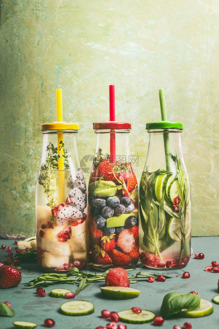 各种五颜六色的水注入瓶与水果浆果,黄瓜,草药饮料吸管与配料桌子上,正视图美味的夏季清洁饮料,健康的生活方式健身图片