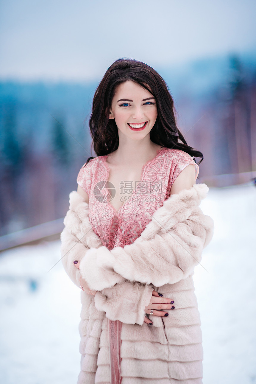 冬山背景上栗色头发蓝色眼睛粉红色连衣裙的女孩图片