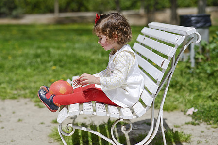 可爱的小女孩坐公园的长凳上玩球图片