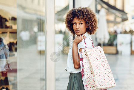 轻的黑人妇女商业街的商店橱窗前非洲女孩,留着AFRO发型,穿着休闲服图片