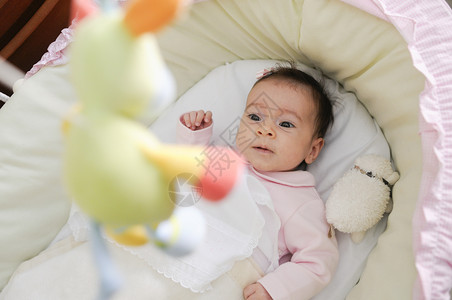 两个月大的女婴看着婴儿床上的洋娃娃图片
