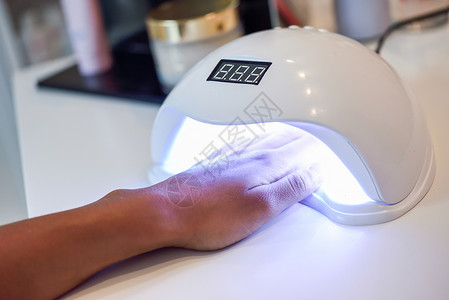 紫外线灯中修剪指甲小指甲艺术美甲业务韦恩斯沙龙的女人的手图片