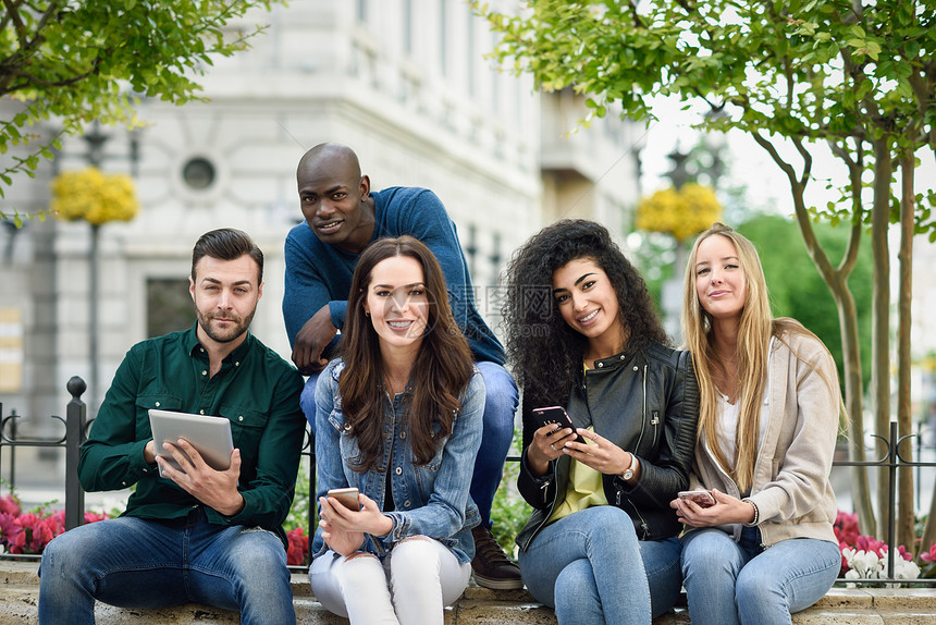 城市背景下用智能手机平板电脑的多民族轻人群体女人男人街上笑着,穿着便装图片