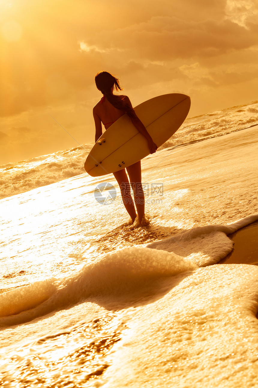 后视镜美丽感的轻女子冲浪女孩穿着比基尼,白色冲浪板日落日出的海滩上走进海浪图片