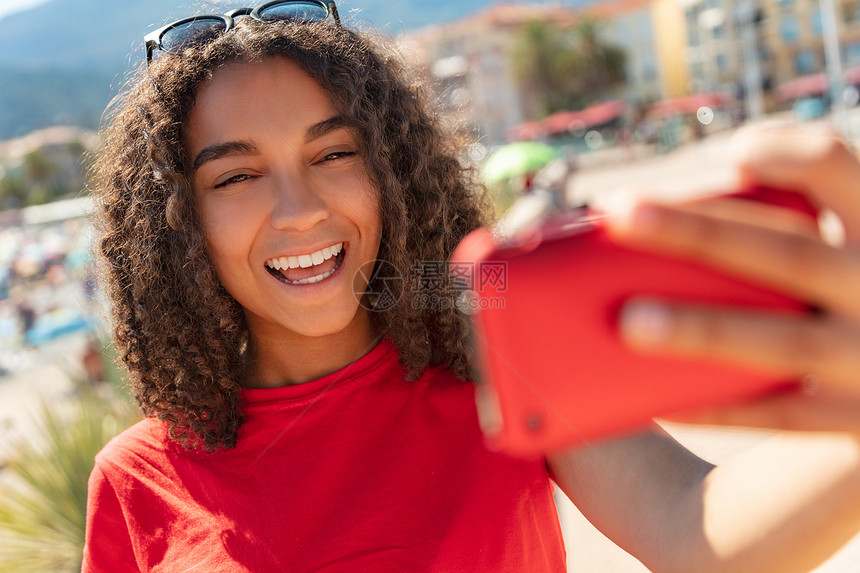 美丽的快乐混合种族非裔美国轻女子少女女孩子微笑与完美的牙齿拍摄自拍照片与红色手机图片