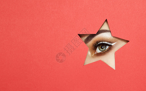 星星眼睛轻美丽的女人的眼睛着明亮的金色阴影富表现力的眉毛,用彩色纸看着星星形状的图案明星诞图案红纸背景