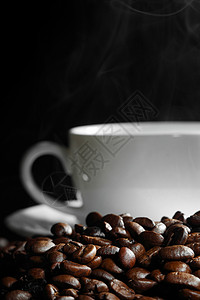 黑色背景的咖啡豆上的杯热气腾腾的咖啡图片