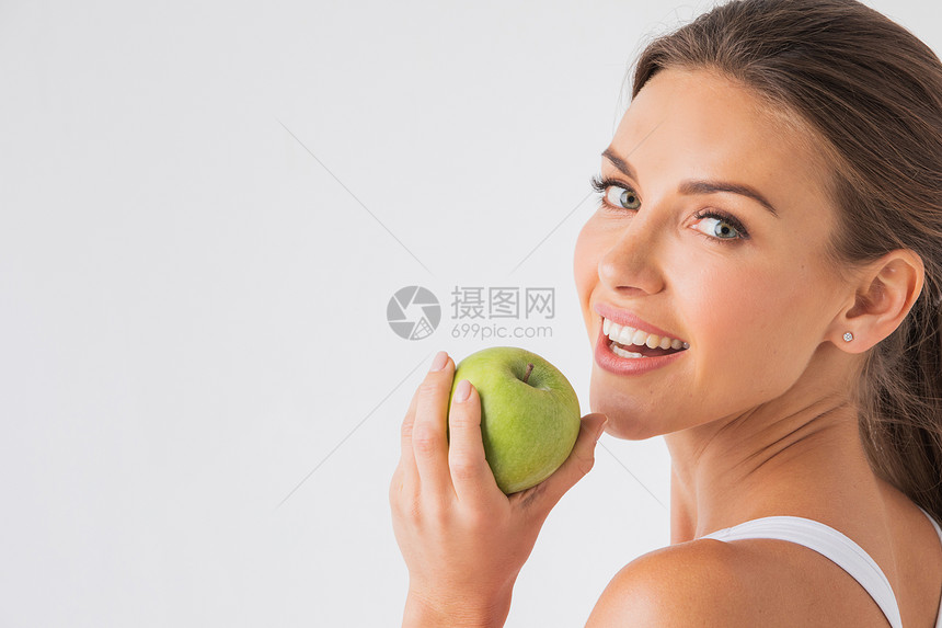 美丽的女人,健康的白牙,白色的背景上着绿色的苹果着绿色苹果的女人图片