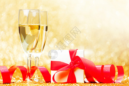 香槟杯,并呈现白色盒子与红色丝带黄金背景图片
