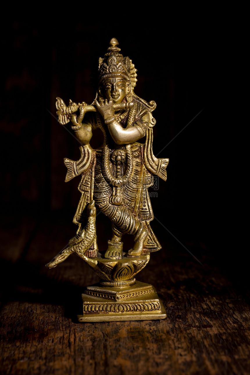 奎师那神毗湿奴化身黄铜雕像隔离木制背景上木背景上的克里希纳雕像图片