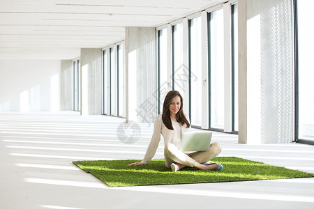 轻的女商人,着笔记本电脑坐空荡荡的办公室里的草坪上图片