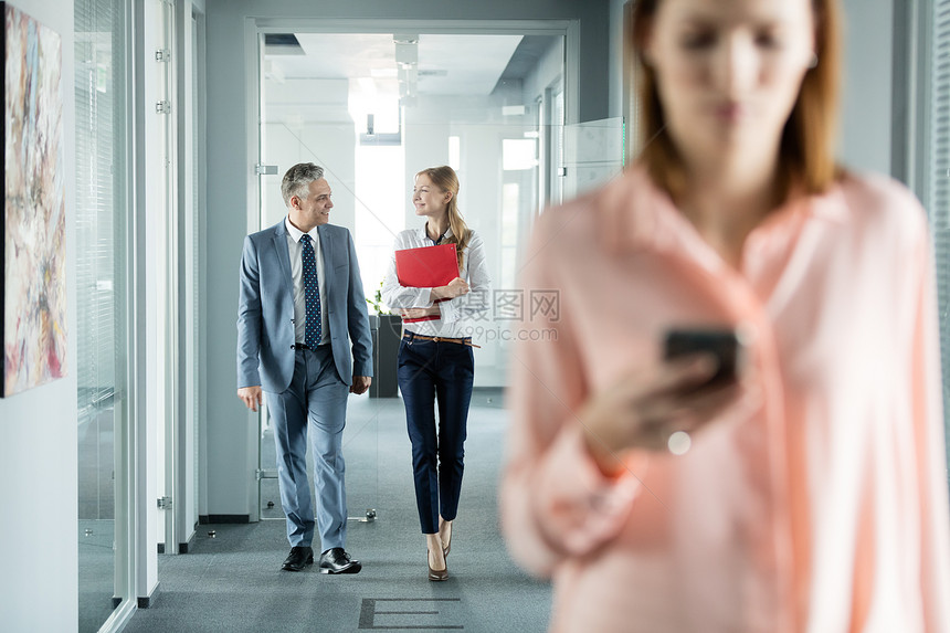 商务人士办公室走廊散步,女同事前台用手机图片