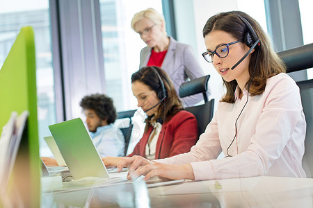 女客户服务代表用笔记本电脑,而同事办公室背景图片