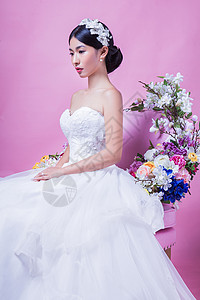 优雅的新娘边看着边坐粉红色背景的椅子上图片