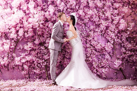 婚礼夫妇亲吻白色的侧视,站墙上,覆盖着粉红色的花图片