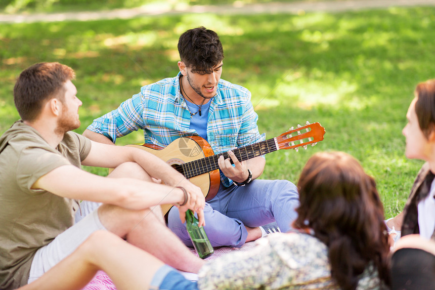友谊,休闲夏季群快乐的微笑朋友与吉他非酒精啤酒冷野餐毯夏季公园朋友们夏天的公园野餐时弹吉他图片