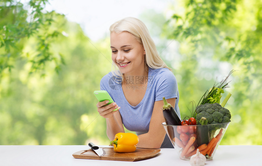 健康的饮食,食物技术微笑的轻妇女与智能手机烹饪蔬菜绿色自然背景微笑的女人用智能手机烹饪蔬菜图片