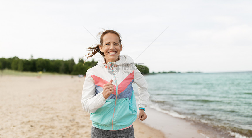 运动,技术健康的生活方式微笑的女人与健身跟踪跑海滩上健身追踪器的女人沿着海滩跑步图片
