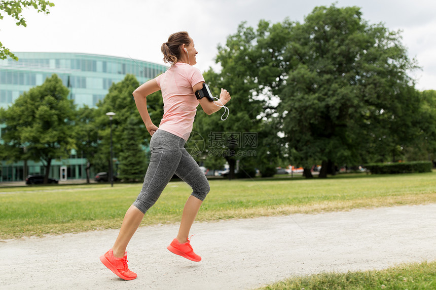 健身,运动健康的生活方式微笑的女人戴着带智能手机的,公园慢跑听音乐带耳机的女人公园里增加慢跑图片