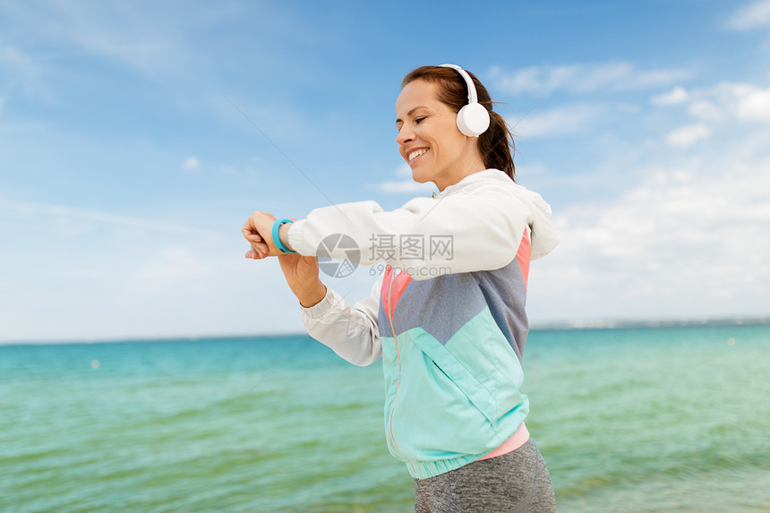 运动,技术健康的生活方式微笑的女人带着耳机健身追踪器海滩上锻炼海滩上戴着耳机健身追踪器的女人图片