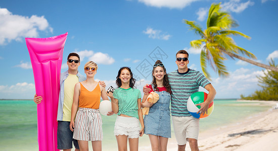 旅游旅游暑假群快乐的微笑朋友戴着太阳镜,带着沙滩球毛巾照相机气垫,异国情调的热带海滩上,以棕榈树为背景快图片