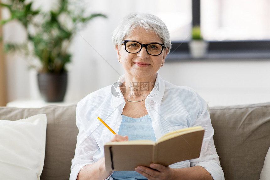 龄,休闲人的快乐的老妇女戴着眼镜,家里写笔记本日记长的女人家写笔记本日记图片